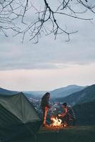 migliore modo per mantenere voi caldo. bellissimo giovane coppia riscaldamento su di il fuoco di bivacco mentre campeggio nel il montagne foto