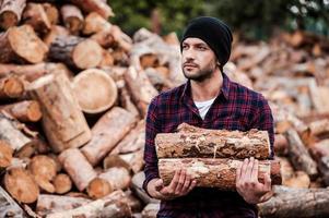 godendo il suo opera con Di legno. fiducioso giovane guardia forestale Tenere logs e guardare lontano mentre in piedi all'aperto foto