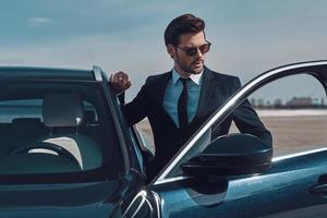 lusso stile. bello giovane uomo d'affari entrata il suo auto mentre in piedi all'aperto foto