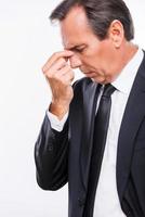 stressato e sovraccarico di lavoro. lato Visualizza di frustrato giovane uomo nel vestito formale toccante il suo naso con mano e conservazione occhi chiuso mentre in piedi isolato su bianca sfondo foto