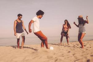 spiaggia sfera. gruppo di allegro giovane persone giocando con calcio palla su il spiaggia con mare nel il sfondo foto