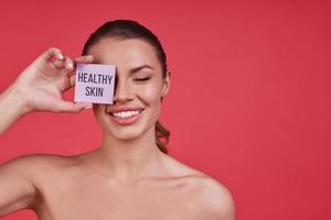 puro bellezza. bellissimo giovane donna sorridente e conservazione occhi chiuso mentre in piedi contro rosa sfondo foto