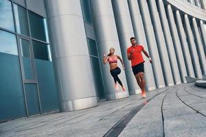 pieno lunghezza di giovane bellissimo donna e uomo nel gli sport capi di abbigliamento godendo mattina jogging mentre praticante all'aperto su il città strada foto