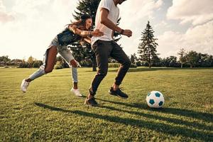 gioco ottenere più caldo. attraente giovane donna e moderno uomo nel casuale indossare in esecuzione mentre giocando calcio all'aperto foto