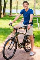 equitazione nel parco. pieno lunghezza di bello giovane uomo equitazione bicicletta nel parco e sorridente foto