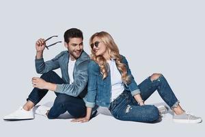 guardare Perfetto. bellissimo giovane coppia nel denim indossare bonding e sorridente mentre seduta contro grigio sfondo foto