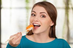 dipendente per Sushi. bellissimo giovane donna mangiare Sushi e sorridente mentre seduta a il ristorante foto