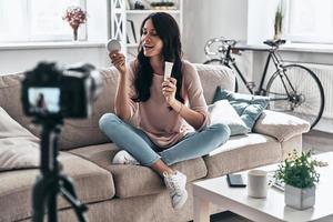 condivisione impressioni. femmina vlogger fabbricazione sociale media video e sorridente mentre seduta in casa foto