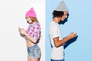 opposti attirare. impaurito giovane coppia Tenere mobile telefoni e in piedi indietro per indietro mentre in piedi contro colorato sfondo foto