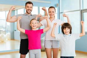 orgoglioso per essere forte e sano. contento sportivo famiglia mostrando loro bicipite e sorridente mentre in piedi vicino per ogni altro nel gli sport club foto