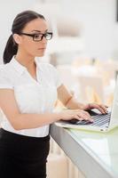 lei è un esperto nel ristorante attività commerciale. bellissimo giovane donna nel vestito formale Lavorando su il computer portatile e mentre pendente a bar contatore foto