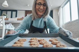 contento anziano donna sorridente mentre preparazione biscotti nel il cucina foto