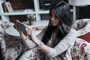 assunzione immagine di... attraente giovane sorridente donna Fotografare qualcosa di sua inteligente Telefono mentre seduta nel ristorante foto