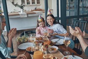 contento famiglia festeggiare compleanno di poco ragazza mentre seduta a il cenare tavolo a casa foto