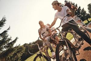 divertimento tempo con Bici. gruppo di contento giovane persone nel casuale indossare sorridente mentre Ciclismo insieme all'aperto foto