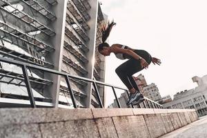 salto più alto. pieno lunghezza di moderno giovane donna nel gli sport capi di abbigliamento salto mentre esercizio all'aperto foto