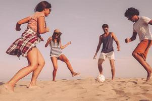 appena avendo divertimento. gruppo di allegro giovane persone giocando con calcio palla su il spiaggia con mare nel il sfondo foto