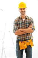 uomo per qualunque lavoro. gioioso giovane costruttore conservazione braccia attraversato e sorridente mentre in piedi in casa foto