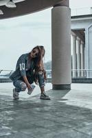 sempre nel stile. bellissimo giovane donna nel jeans indossare conservazione mano nel capelli e Tenere un' monouso tazza mentre la spesa tempo all'aperto foto