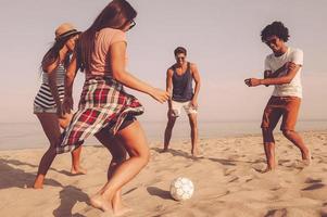 spiaggia calcio. gruppo di allegro giovane persone giocando con calcio palla su il spiaggia con mare nel il sfondo foto