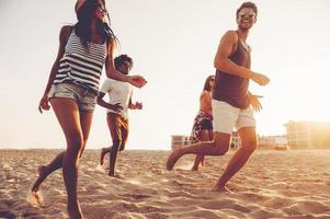 giovane sera fare jogging. gruppo di giovane allegro persone in esecuzione di il spiaggia e guardare contento foto