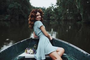 godendo spensierato giorno. bellissimo giovane donna nel elegante vestito sorridente mentre seduta nel il barca foto