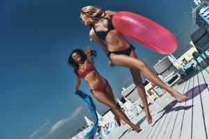 pieno lunghezza di Due bellissimo giovane donne nel bikini sorridente mentre in esecuzione vicino il piscina insieme foto