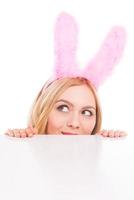 curioso Pasqua coniglietto. bellissimo giovane biondo capelli donna con coniglio orecchie guardare su di copia spazio e contro bianca sfondo foto