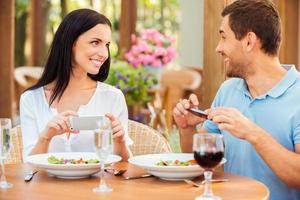 cattura loro tempo insieme. contento giovane amorevole coppia assunzione immagini di loro cibo e sorridente mentre rilassante nel all'aperto ristorante insieme foto