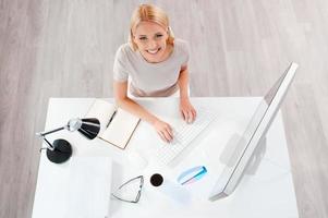 donna d'affari a Lavorando posto. superiore Visualizza di bellissimo giovane biondo capelli donna Lavorando a il computer e guardare a telecamera mentre seduta a sua Lavorando posto foto