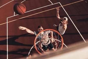 Due giovane uomini nel gli sport capi di abbigliamento giocando pallacanestro e sorridente mentre la spesa tempo all'aperto foto