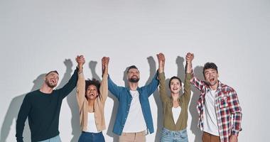 gruppo di allegro giovane persone nel casuale capi di abbigliamento Tenere mani stretto e guardare su foto