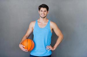 siamo voi pronto per il gioco contento giovane muscolare uomo Tenere pallacanestro palla mentre in piedi contro grigio sfondi foto