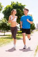 jogging insieme. pieno lunghezza di giovane donna e uomo nel gli sport capi di abbigliamento in esecuzione lungo il strada foto