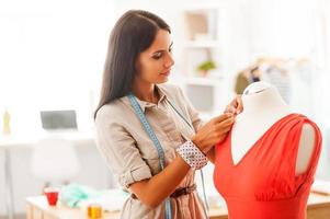 perfezionamento il stile. bella giovane donna pinning tessile su vestito mentre in piedi nel sua moda laboratorio foto