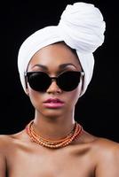 fiducioso nel sua stile. bellissimo africano donna indossare un' foulard e guardare a telecamera mentre in piedi contro nero sfondo foto