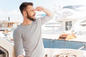 apertura nuovo orizzonti. fiducioso giovane uomo guardare inoltrare e sorridente mentre in piedi su il tavola di yacht foto