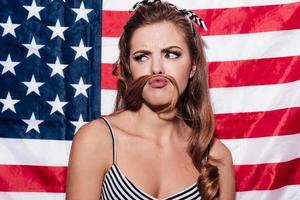 Guarda a mio baffi ritratto di giovane donna fabbricazione falso baffi Guarda astuzia in piedi contro americano nazionale bandiera foto