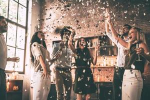 godendo luminosa momenti. gruppo di contento giovane persone lancio coriandoli e salto mentre godendo casa festa su il cucina foto