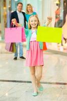 famiglia acquisti. allegro famiglia shopping nel shopping centro commerciale mentre poco ragazza mostrando sua shopping borse e sorridente foto