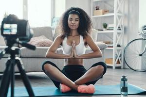 bellissimo giovane africano donna seduta nel il yoga posizione mentre fabbricazione sociale media video foto
