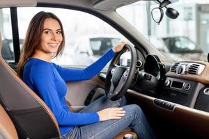 aderire me per un' viaggio. attraente giovane donna seduta a il davanti posto a sedere di il auto guardare a telecamera foto