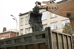 strada lavori su il città strada. il scavatrice secchio raccoglie il vecchio marciapiede e carichi esso in un' cumulo di rifiuti camion foto