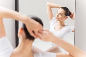 qualunque cosa dovrebbero essere Perfetto. bellissimo giovane ballerina regolazione sua capelli mentre seduta contro specchio e guardare a sua riflessione foto