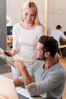 chiede per un esperto consiglio. allegro giovane uomo e donna discutere qualcosa e guardare a digitale tavoletta insieme mentre loro colleghi Lavorando nel il sfondo foto