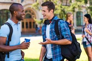 chat con gli amici. Due giovane uomini parlando per ogni altro e sorridente mentre Due donne in piedi nel il sfondo foto