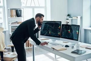 concentrato giovane uomo nel camicia e cravatta scrittura qualcosa giù e parlando su il Telefono mentre Lavorando nel il ufficio foto