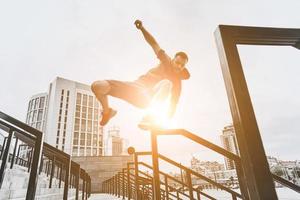 formazione per diventare il migliore. Basso angolo Visualizza di bello giovane uomo nel sport capi di abbigliamento salto al di sopra di ringhiera mentre esercizio al di fuori foto