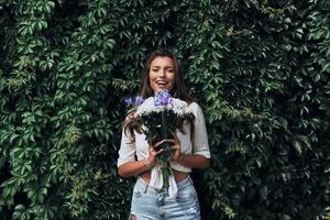 per sempre giovane e Bellissima. attraente giovane donna guardare a telecamera e sorridente mentre in piedi all'aperto foto