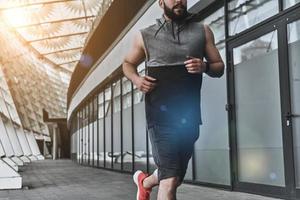 appena mantenere in movimento. vicino su di giovane uomo nel sport capi di abbigliamento in esecuzione mentre esercizio al di fuori foto